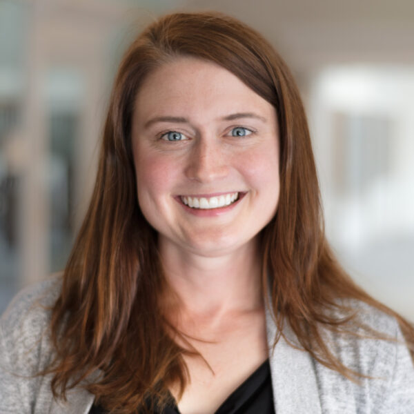 http://Headshot%20of%20Ashley%20Champagne%20from%20the%20shoulders%20up%20smiling%20in%20black%20top%20and%20grey%20cardigan.