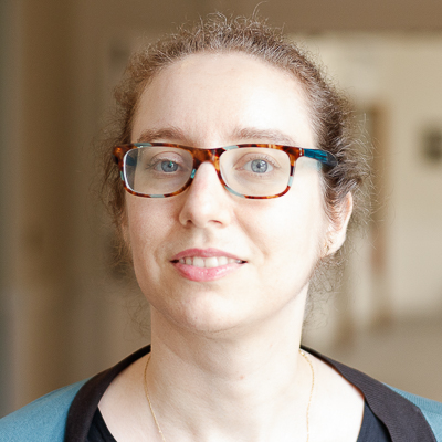 http://Headshot%20of%20Elizabeth%20Yalkut%20from%20the%20shoulders%20up%20smiling%20in%20blue%20cardigan%20with%20glasses.